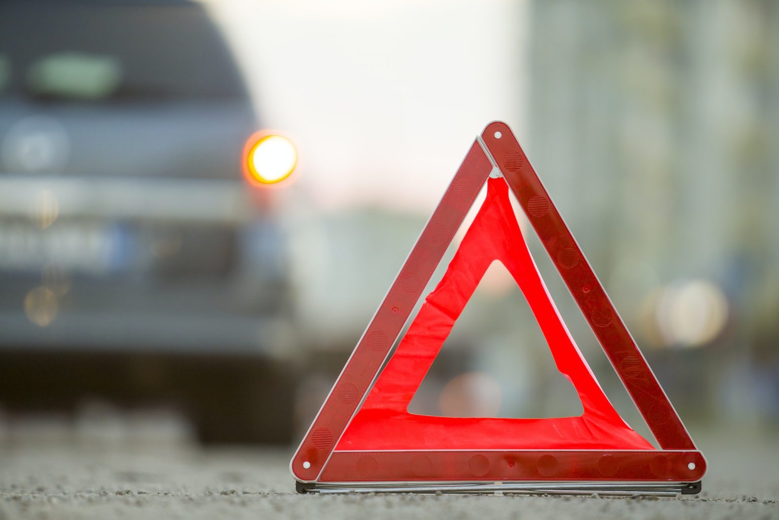 Red emergency triangle stop sign and broken car on a city street
